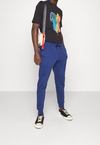 Blue jogger pants with elastic waistband and cuffs, paired with a black t-shirt featuring a colorful horse design. Black sneakers completed the outfit.