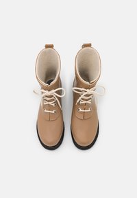 Botas de cuero marrón claro con cordones, forradas con un suave tejido beige, puntera redondeada y suela de goma negra. Cuenta con dos ojetes y una lengüeta en la parte trasera.