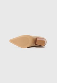 Beige suede shoe with a pointed toe and a block heel. The sole features a ribbed texture. The heel has a glossy finish.