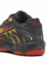 Scarpa sportiva nera con tomaia in mesh, caratterizzata da accenti rossi e gialli. Tacco arrotondato e suola texturizzata per una migliore trazione. Logo Puma visibile.
