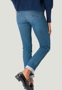 Jean en denim bleu ajusté avec des poignets retroussés, présentant un design classique à cinq poches et des coutures contrastantes sur les poches arrière.