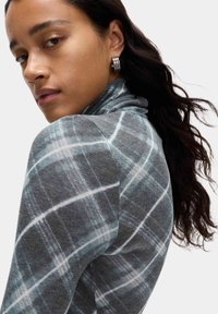 Top a quadri grigi con colletto arrotondato, caratterizzato da linee azzurro chiaro e bianche. Tessuto morbido con silhouette aderente e sottili dettagli di texture.