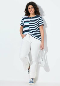 Camiseta de rayas en marino, azul claro y blanco; corte relajado. Combinada con jeans blancos, zapatillas azules y un bolso plateado.