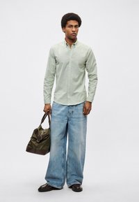 Πράσινο πουκάμισο με κουμπιά και μακριά μανίκια, άνετο, χαλαρό μπλε τζιν, σκούρα παπούτσια και σκούρα τσάντα ώμου σε ελιά απόχρωση. Ομαλή υφή, casual σχεδιασμός.