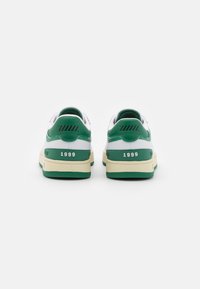 Sneaker verde e bianco con una tomaia testurizzata, dotate di un tab del tallone prominente, l'anno "1999" e una suola beige con accenti verdi.