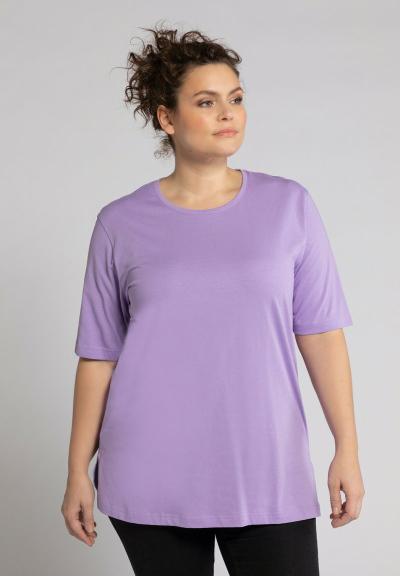 Helllila Kurzarm-T-Shirt aus weichem Material, mit einem runden Ausschnitt und einem lässigen Schnitt, kombiniert mit schwarzen Hosen.