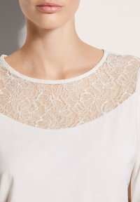 Wit T-shirt met een bloemenkant inzetstuk bij de halslijn, een gladde stof voor het lichaam en een ronde halslijn.