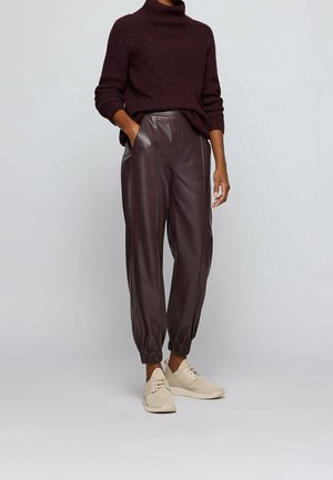 Pull en maille violette foncée surdimensionné, associé à un pantalon en cuir marron taille haute et fuselé, et des baskets beiges. Texture douce et coupe décontractée.