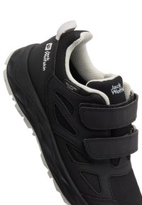 Black athletic shoe with a Velcro strap design, textured synthetic upper, mesh accents, and a white rubber sole. Logo visible on side.