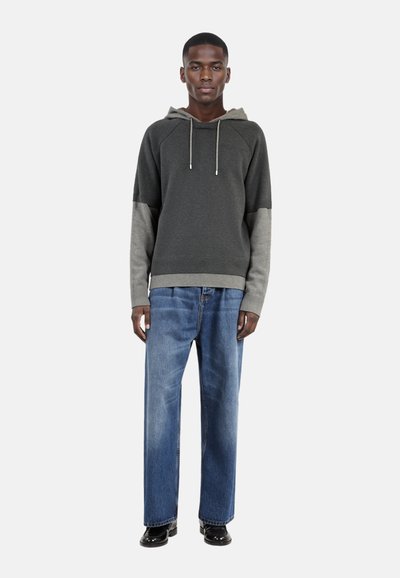 Felpa grigia con cappuccio e maniche grigie chiare, orlo a costine e coulisse, abbinata a jeans blu chiaro a gamba dritta e scarpe nere.