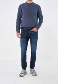 Námořnicky modrá košile s dlouhým rukávem a henley límcem se třemi knoflíky, doplněná tmavě modrými džínami a šedými sportovními botami.