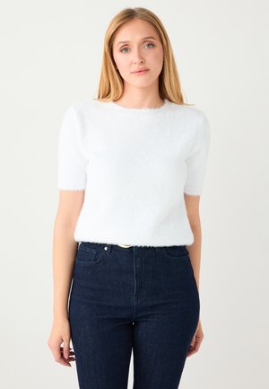 Pull blanc à manches courtes et duvetées avec un col rond, associé à un jean taille haute bleu foncé. Texture douce, coupe décontractée.