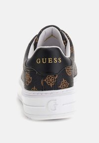 Sneaker in pelle nera con motivi geometrici marroni, suola bianca e tallone nero con la scritta "GUESS" in lettere dorate.