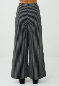 Hoge zwarte broek met witte verticale strepen, gezien vanaf de achterkant, met wijde benen en een getailleerde pasvorm.