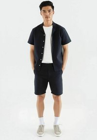 Kortermet mørk mønstret skjorte, hvit T-skjorte med rund hals, matchende mørke shorts, lysegrå sneakers og hvite sokker.