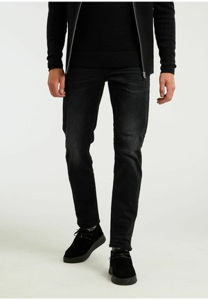 Chaqueta negra con cremallera sobre un suéter negro texturizado, combinada con jeans negros ajustados y zapatos de ante negros. Diseño simple y elegante.