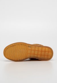 Semelle d'une chaussure marron avec une semelle extérieure en caoutchouc translucide présentant des motifs de semelle ondulés et en grille sur un fond blanc.