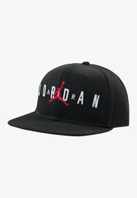 Svart snapback-cap laget av bomull med strukturert design. Har brodert "JORDAN"-bokstaver og en rød Jumpman-logo på fronten.