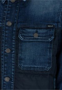 Takkatakki tummansinisestä denimistä, metallinapeilla, rintataskulla ja vuorattuna tikatulla sisällä. Sisältää "REPLAY" logo-tagin. Karhea kangas.