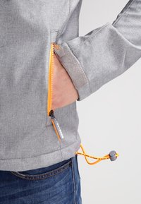 Grijze stoffen jas met oranje ritsen en trekkoord. Heeft een zijzak en een gladde textuur, ontworpen voor comfort en functionaliteit.