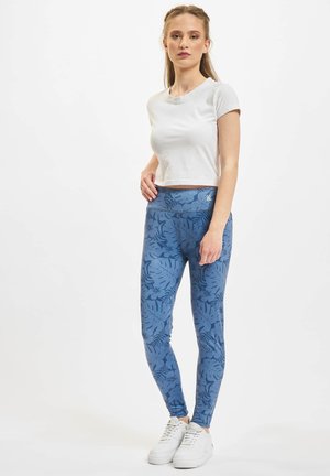 Leggings azules con un patrón de hojas, hechos de un material elástico. Combinados con una blusa blanca de manga corta y zapatillas blancas.