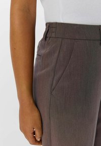 Pantalon marron ajusté avec une finition texturée. Comprend des poches latérales et une taille plate avec des plis discrets pour des détails supplémentaires.
