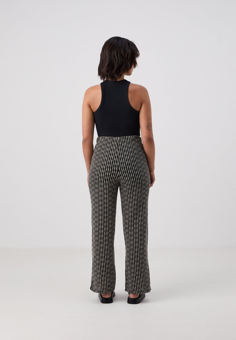 Black sleeveless top paired with high-waisted, wide-leg pants featuring a black and white textured pattern. Smooth fabric with subtle sheen.