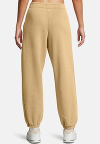 Beiga sweatpants med avslappnad passform, elastisk midja och smalnande cuffs. Slät textur, inga synliga mönster. Kombineras med vita sneakers.