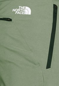 Zielone materiałowe spodnie z zamkiem błyskawicznym w kieszeni, dyskretnym przeszyciem i logo The North Face w kolorze białym na górnej części.