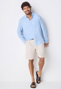 Hele sinine linane särk pikkade varrukatega, beežid lühikesed püksid ja tume libisevad sandaalid. Lihtne disain, särgil on tasku, lõdva lõikega.