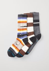 Tres pares de calcetines: uno con franjas multicolores en naranja y azul, uno a rayas en marrón y blanco, y uno gris acanalado.