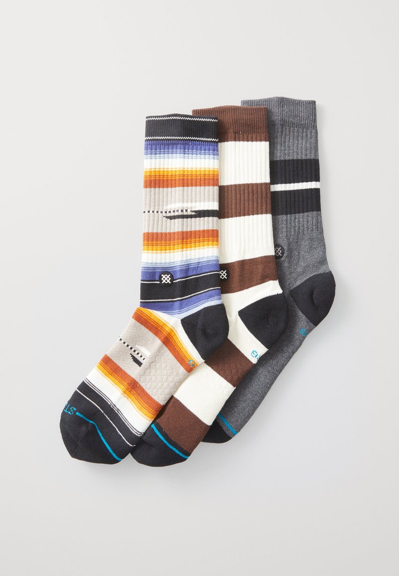 Tres pares de calcetines: uno con franjas multicolores en naranja y azul, uno a rayas en marrón y blanco, y uno gris acanalado.