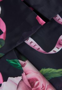 Schwarzer Stoff mit einem floralen Muster aus pinken Rosen und grünen Blättern. Akzentuiert mit einem Band, auf dem das Wort "BAKER" gedruckt ist.