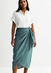 White button-up shirt with short sleeves and two chest pockets, paired with a teal, textured wrap skirt featuring a knot detail.