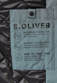 Oznaka za njegu od recikliranog poliestera na kviltanoj tamnoj tkanini, koja sadrži detalje otporne na vodu i upute za njegu. Boje: crna i svijetlo plava.