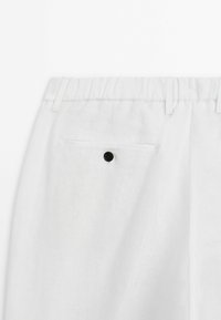 Weiße Leinenhosen mit strukturiertem Oberflächen, ausgestattet mit einem elastischen Bund, einer Gesäßtasche mit einem schwarzen Knopf und einem taillierten Schnitt.