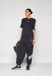 Μαύρο αθλητικό σύνολο που αποτελείται από ένα φαρδύ t-shirt και στενά joggers με λευκές ρίγες τριπλής γραμμής και λογότυπα.