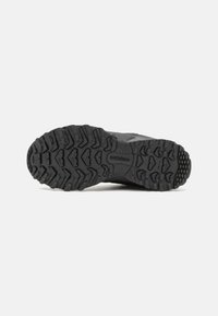 Black hiking shoe sole with deep tread patterns, textured rubber material, and New Balance branding; designed for traction and stability.