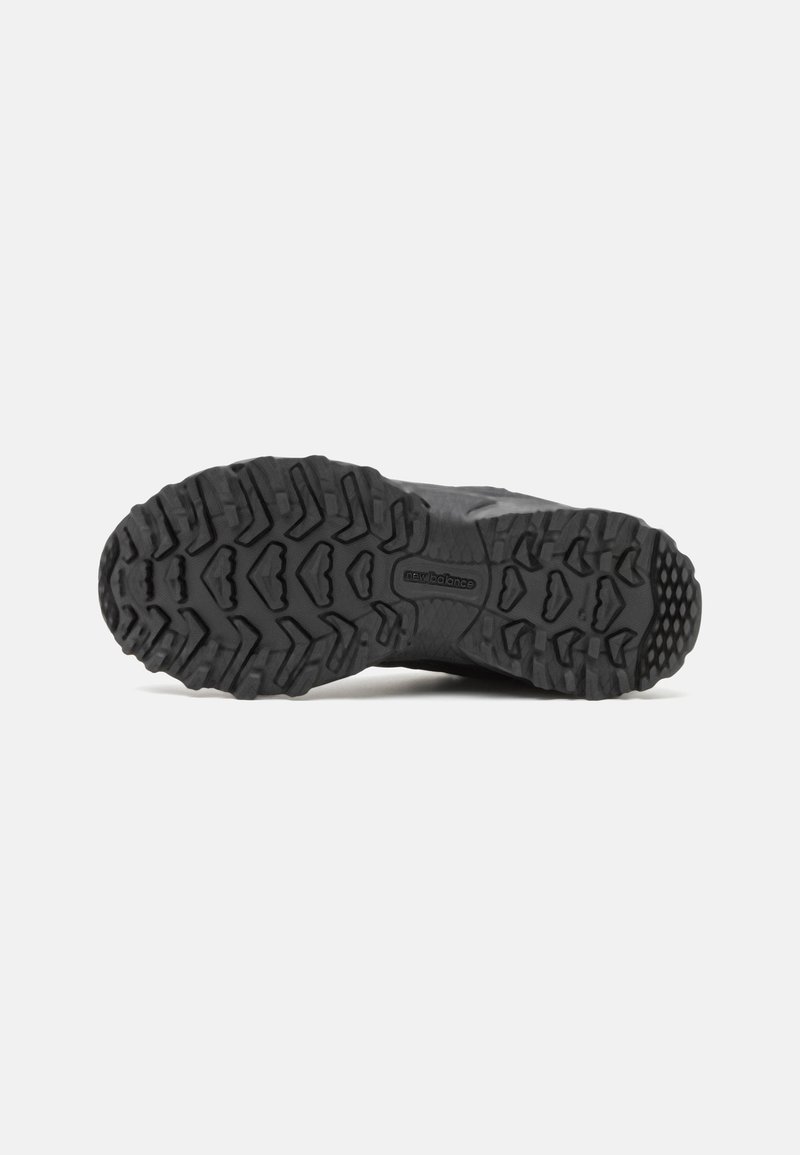 Schwarze Wanderschuhsohle mit tiefen Profilmustern, strukturiertem Gummi-material und New Balance-Logo; entwickelt für Traktion und Stabilität.