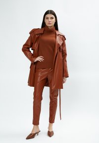 Cappotto trench in finta pelle marrone sopra un dolcevita a righe marrone e pantaloni slim-fit abbinati, abbinato a mule marroni a punta. Tessuto dalla finitura liscia.