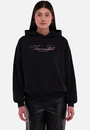 Zwarte hoodie met een losse pasvorm, voorzien van roze geborduurde tekst "Tomorrowsland een magische bijeenkomst" en ribbelboorden aan de mouwen en onderkant.