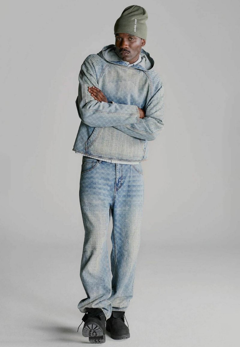 Completo giacca e pantaloni in denim azzurro con motivo a trama. Abbinato a una felpa con cappuccio grigia e calzature nere, include un berretto verde.