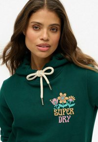Groene hoodie met een koord, versierd met bloemenprints en de tekst "SUPER DRY". Gemaakt van zachte stof, ontworpen voor comfort en warmte.