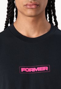 Black cotton t-shirt featuring a crew neck, with a pink rectangular "FORMER" logo stitched on the front.