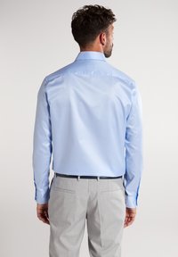 Lichtblauw overhemd met lange mouwen, gladde textuur en getailleerde pasvorm, gecombineerd met lichtgrijze broek en een zwarte riem.