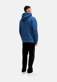 Sudadera azul con capucha, de corte relajado, textura suave y puños acanalados, combinada con pantalones de pana negros y zapatillas blancas.