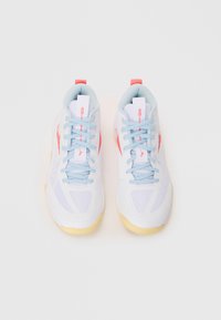 Une paire de chaussures de sport blanches avec des lacets bleu clair, un logo et des onglets de talon corail, et des semelles beige, vue par le dessus sur un fond blanc.
