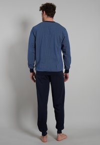 Marineblauer Trainingsanzug mit einer gemusterten Jacke und einfarbigen, dunklen Hosen. Die Jacke hat ein geometrisches Design und gerippte Bündchen.