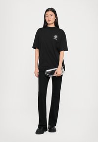T-shirt oversize nera con design grafico sul petto, abbinata a pantaloni neri a campana e una borsa a tracolla argentata. Tessuto morbido e vestibilità comoda.