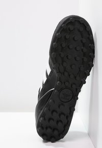 Schwarzer Sportschuh mit einer strukturierten Gummisohle, der weiße Streifen an der Seite aufweist, und einem glatten Leder-Obermaterial mit stikauffen Details.